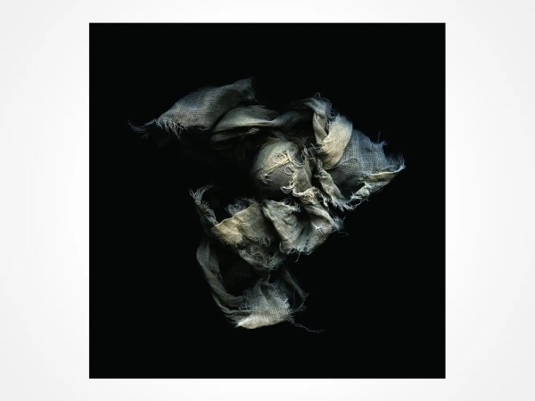 A loosely bundled piece of frayed, textured fabric in shades of gray and beige appears suspended against a solid black background.