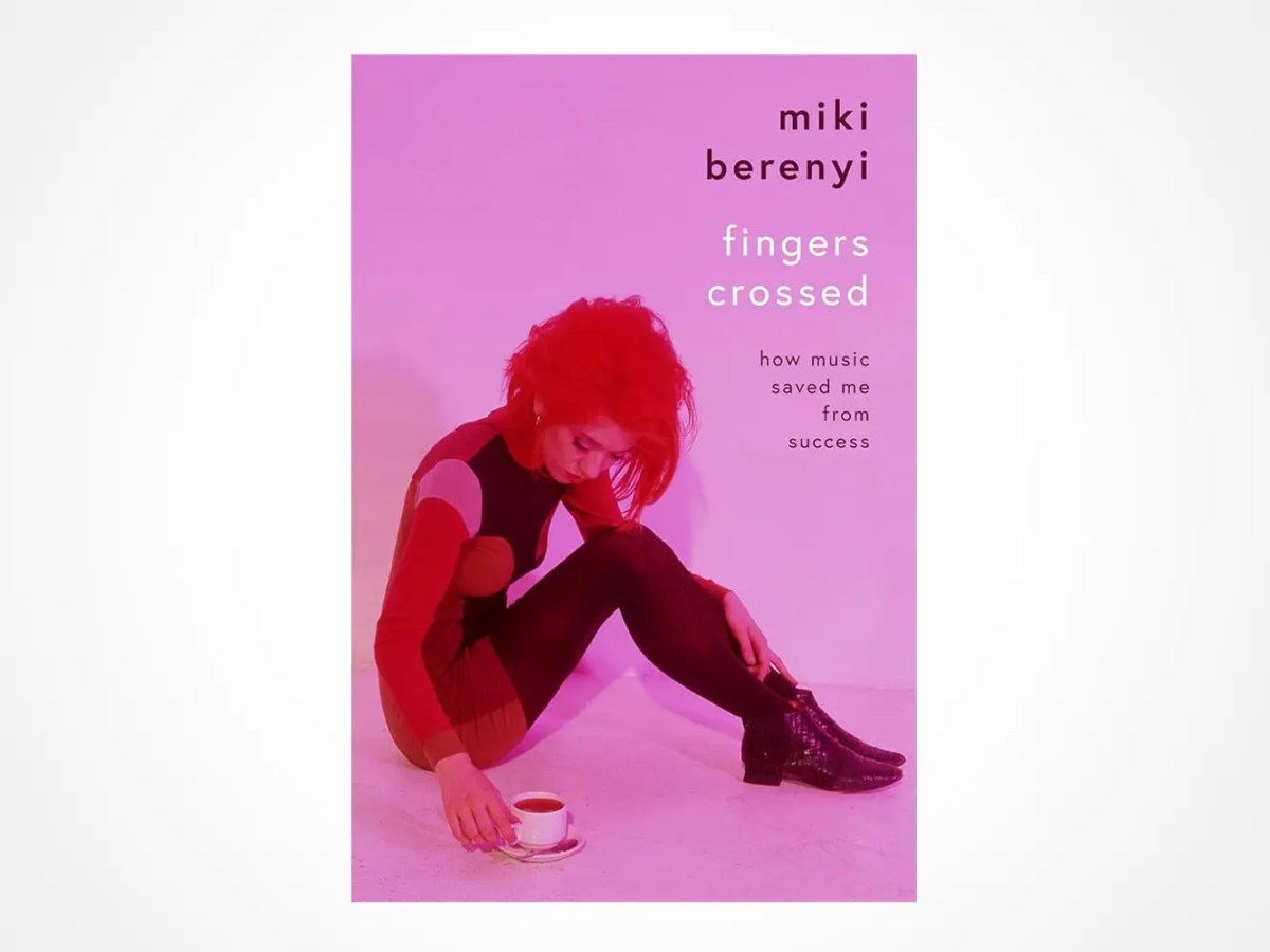 Book cover for Fingers Crossed by Miki Berenyi. A woman with red hair in a red and black outfit crouches on the floor, looking down at a teacup. The background and overall image have a pink tint.